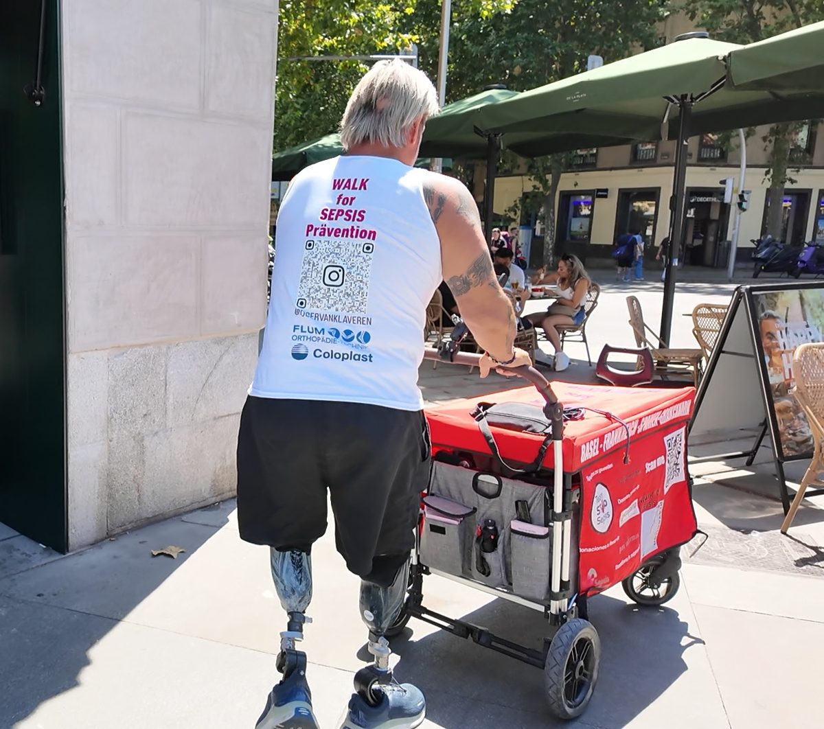 Roger van Klaveren von hinten mit dem bedruckten Bollerwagen vor einem Café in Madrid